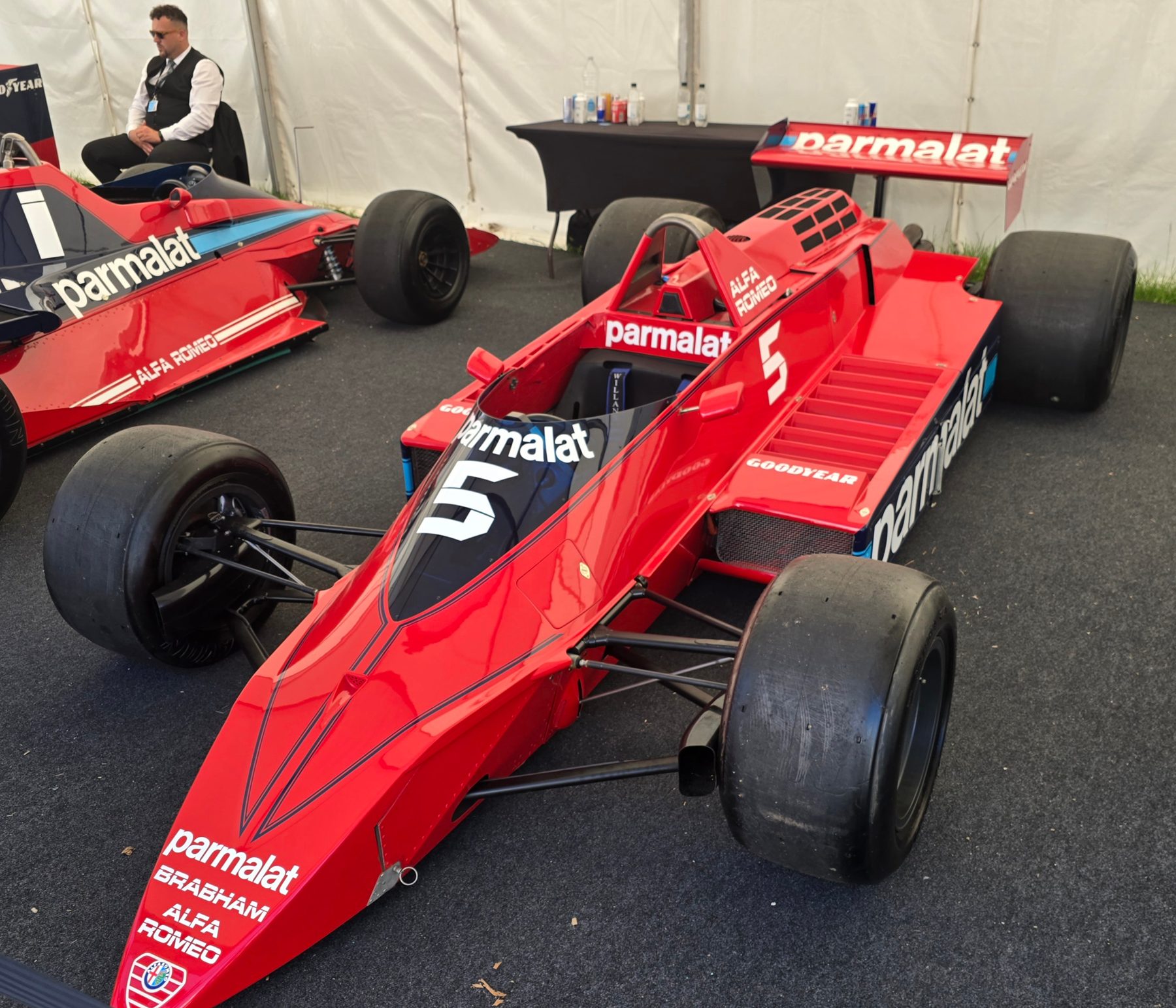 In colour: a red Formula One car with a long pointed nose, No. 5 on the nose and engine cover and Parmalat lettering, seen from the front three-quarter in a white tent; another red car with No. 1 stands behind at the left, an attendant seated beyond it.