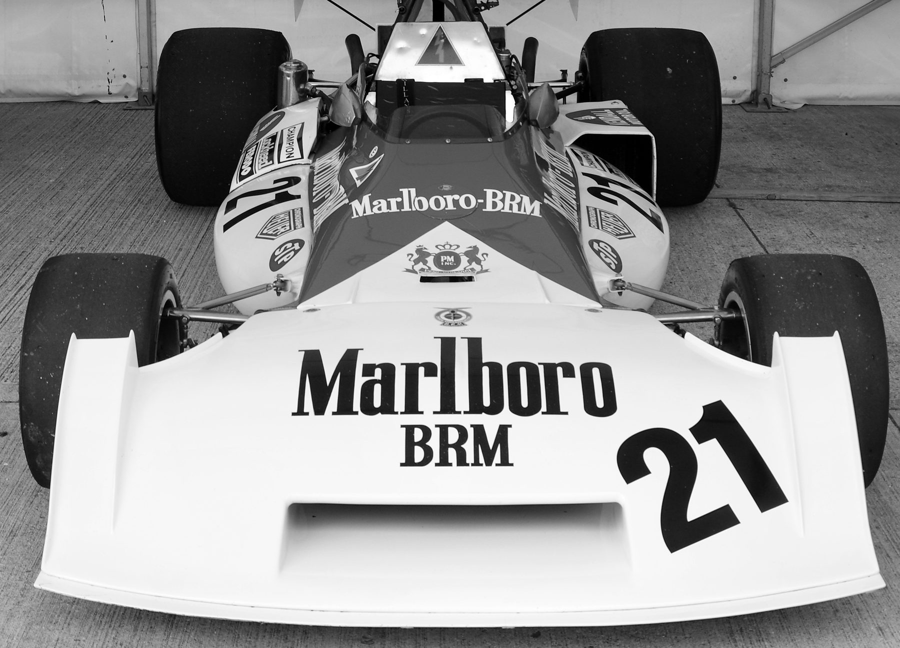 Head-on view of a single-seater with a broad, flat nose carrying a large No. 21 and sponsor lettering, its slick tyres either side, standing on a concrete floor in front of a white tent wall.