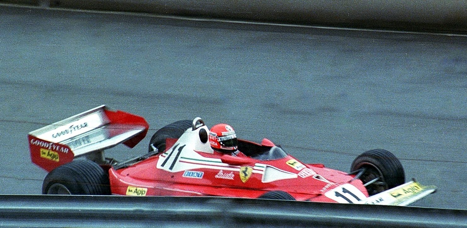 In colour: a red and white racing car numbered 11, with a large white rear wing, passes behind a steel barrier, panned so that the grey track and the wall behind it are streaked with motion blur.