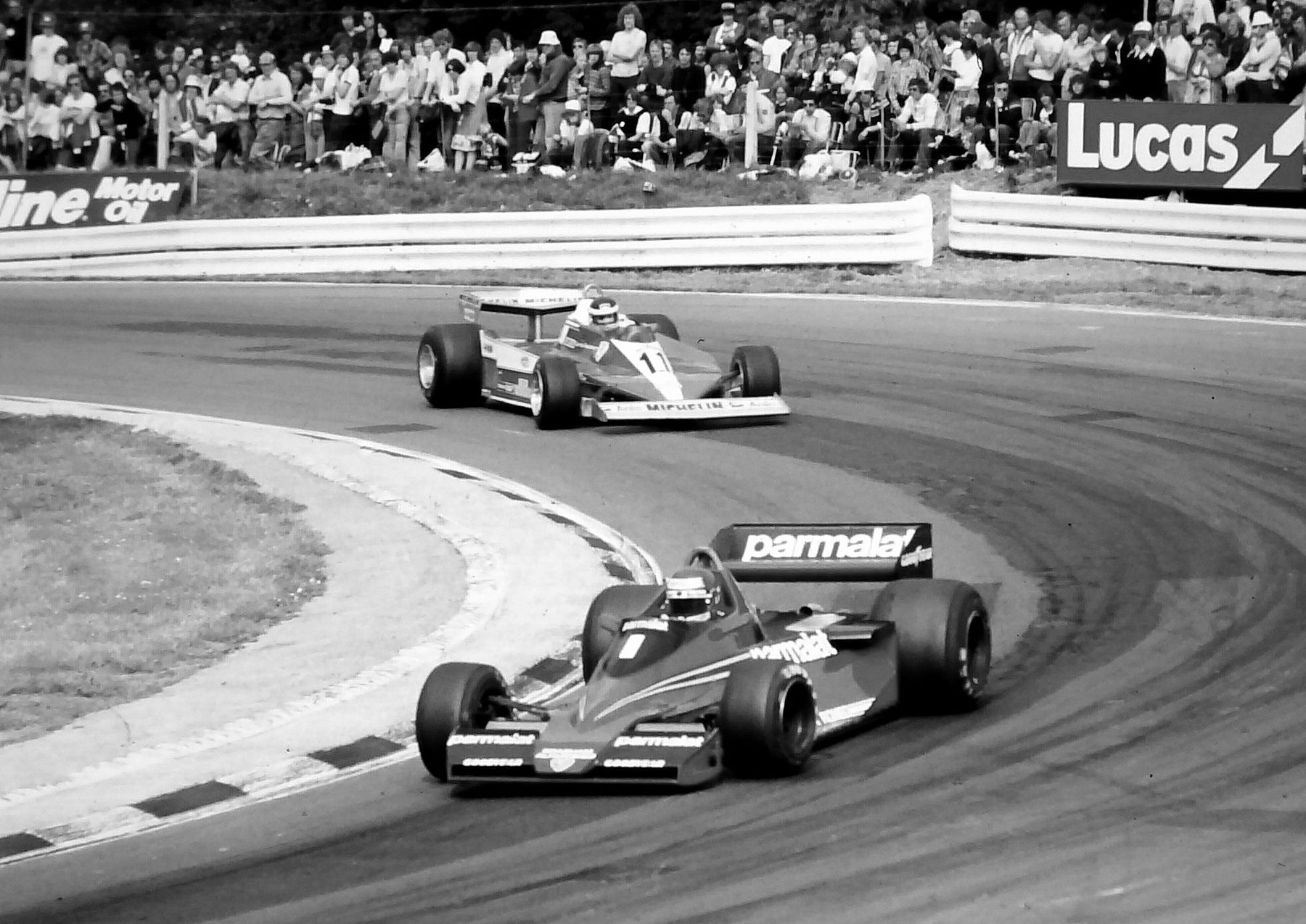 Two single-seaters round a tight hairpin, the nearer numbered 1, the one behind numbered 11; a crowd stands along the bank above the barrier.