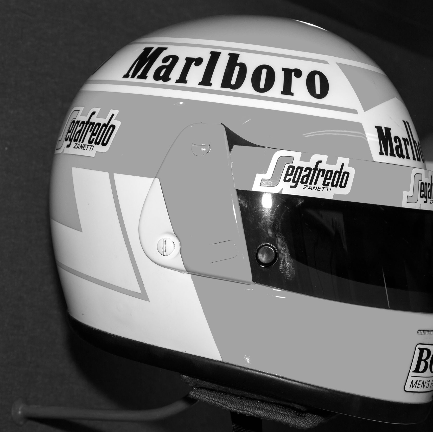 A glossy two-tone full-face racing helmet with sponsor wordmarks on the crown and the sides and a dark visor, displayed on a peg against a dark cloth wall.